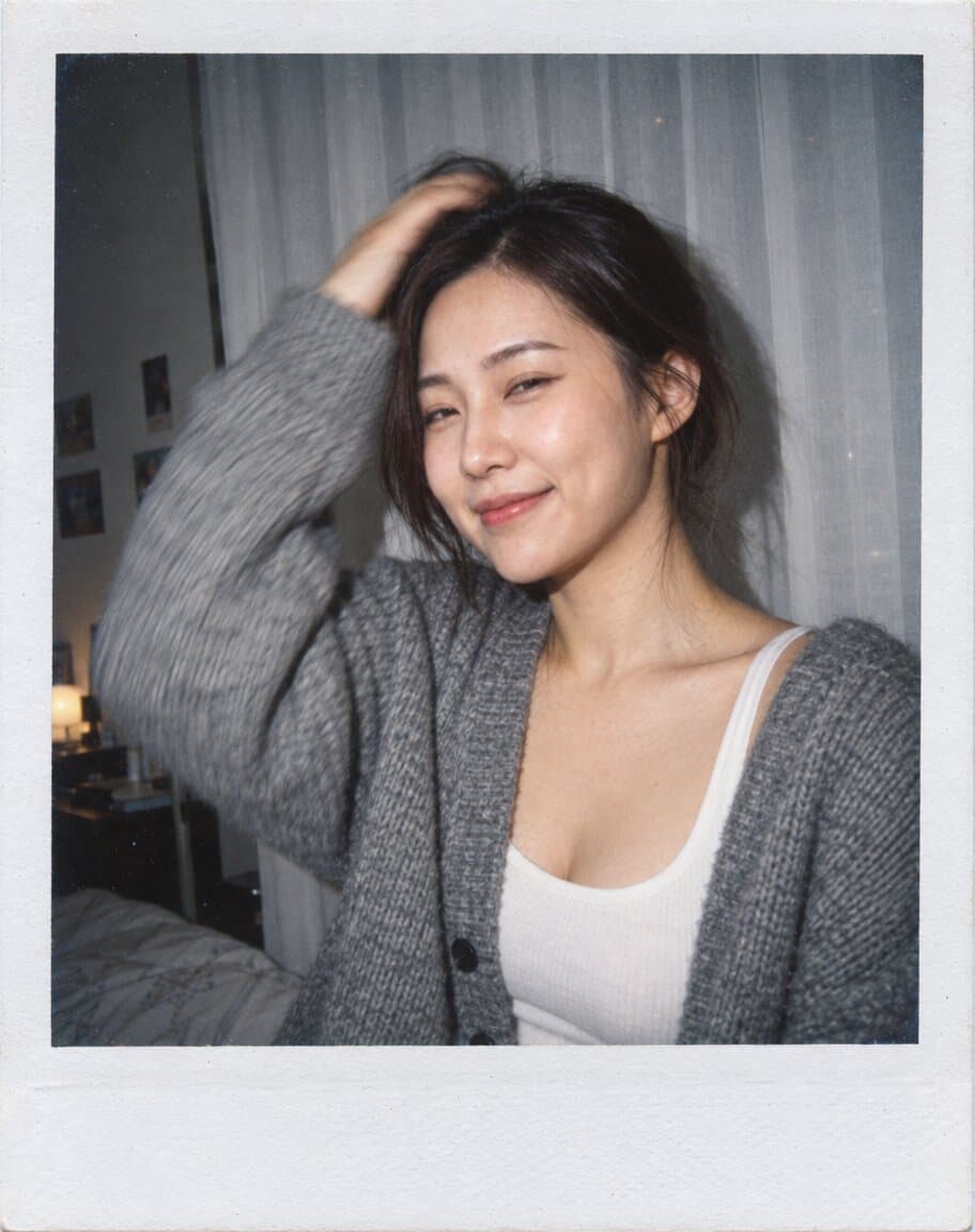 Instant-film style flash photo of a woman laughing in front of a white curtain