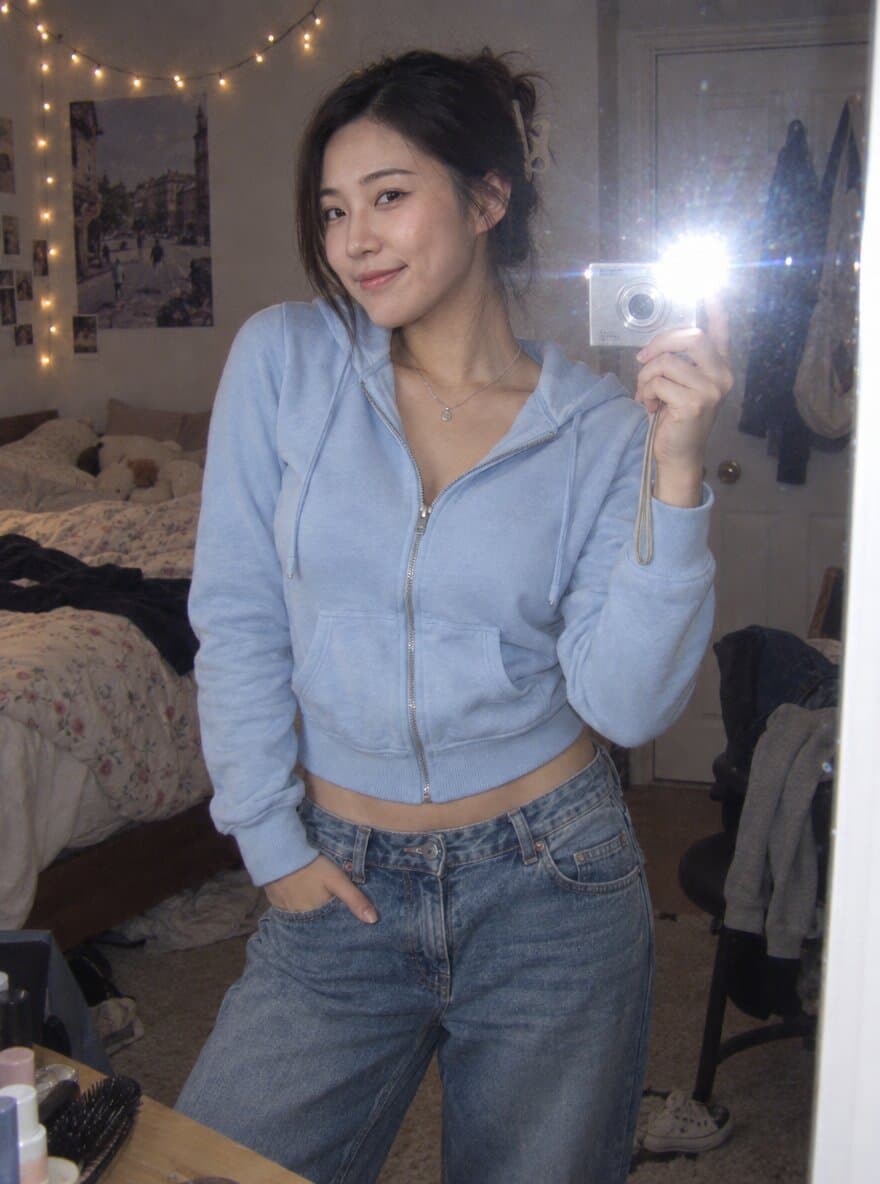 Early-2000s style flash mirror selfie of a woman holding a silver compact digital camera